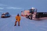 A man in a yellow coat standing in front of snow vehicles