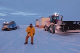 A man in a yellow coat standing in front of snow vehicles