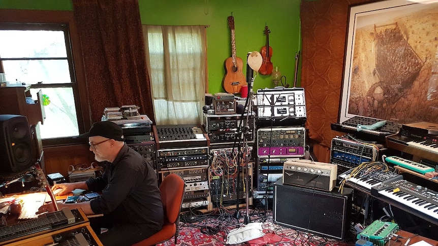 A man in a recording studio surrounded by musical instruments and equipment