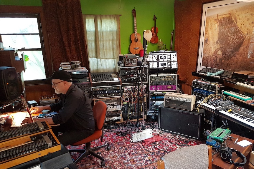 A man in a recording studio surrounded by musical instruments and equipment