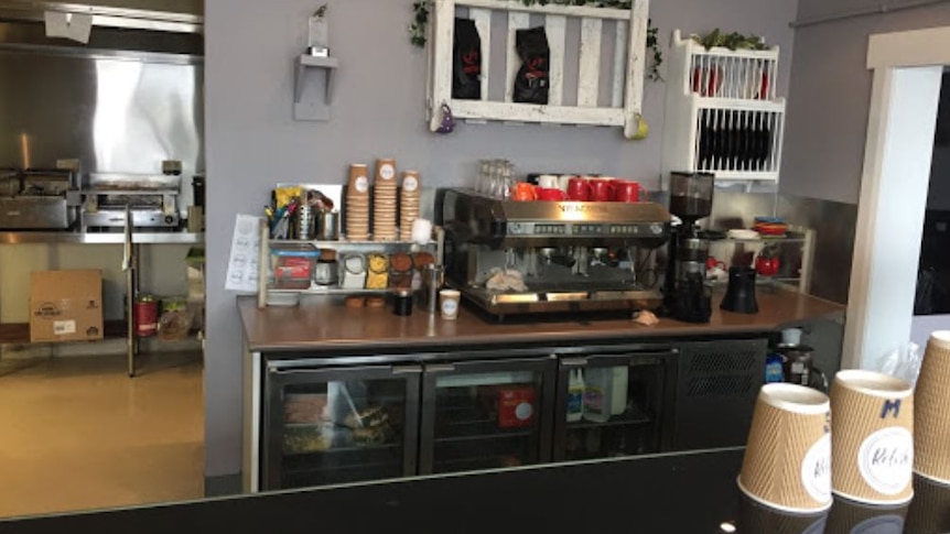 A cafe servery with coffee machine, and cups and a line of fridges.