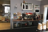 A cafe servery with coffee machine, and cups and a line of fridges.