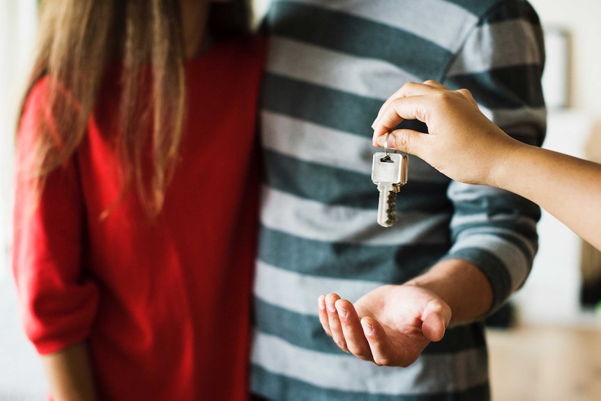 A person handing over keys to a man and a woman