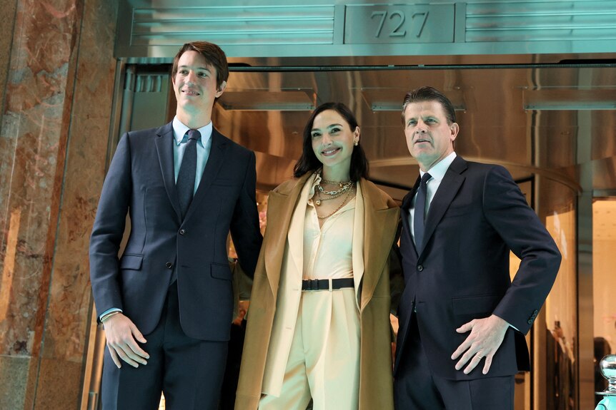 Two men in suits stand next to Gal Gadot 
