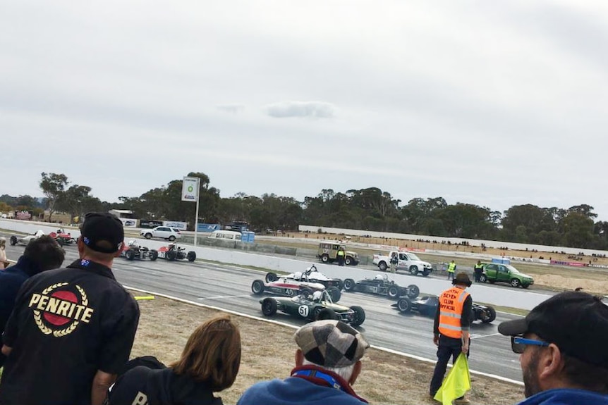 Spectators watch racing cars on track.