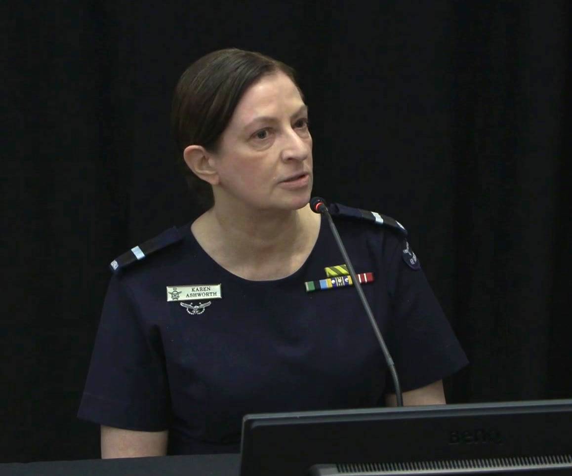 A serious-looking woman in a blue military uniform speaks into a microphone.