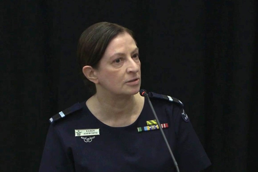 A serious-looking woman in a blue military uniform speaks into a microphone.