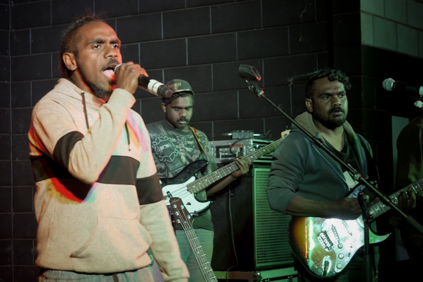 Two Indigenous guitarists and a singer on stage performing.