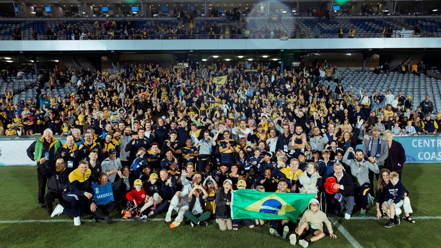 A group celebrating an A-League win on a soccer field.