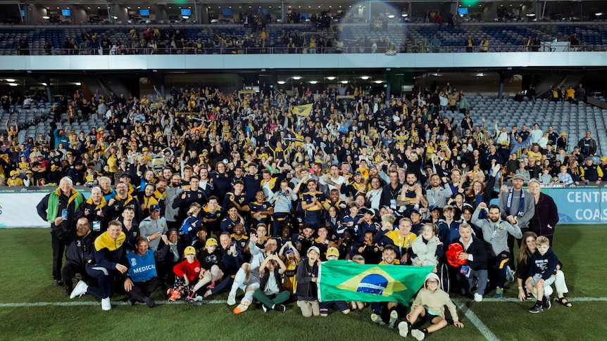 A group celebrating an A-League win on a soccer field.