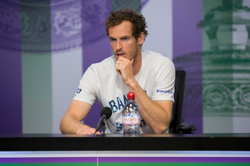 Andy Murray sits at a table to answer questions after his defeat at Wimbledon.