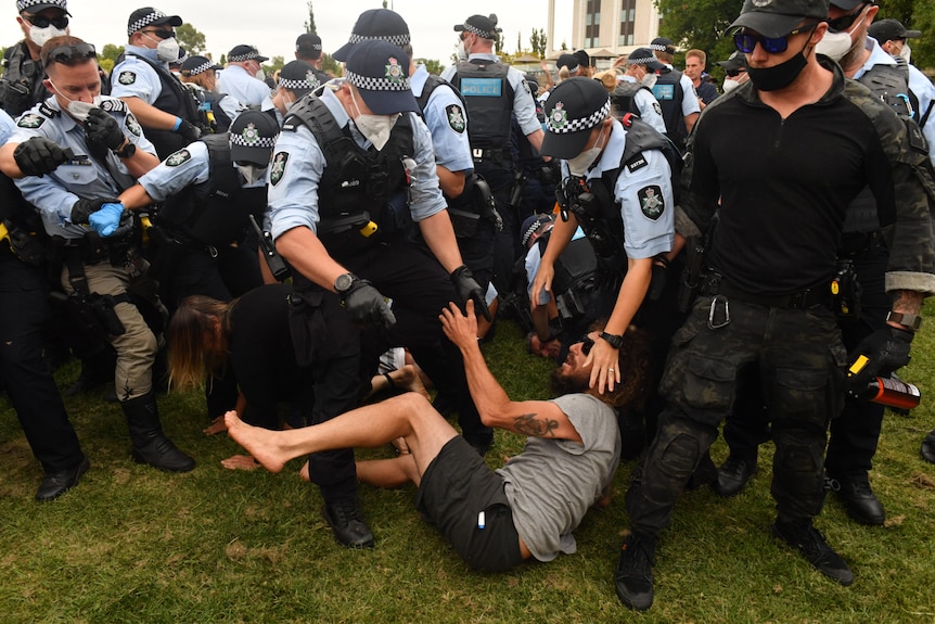 A large number of police stand over a man who is on the ground.