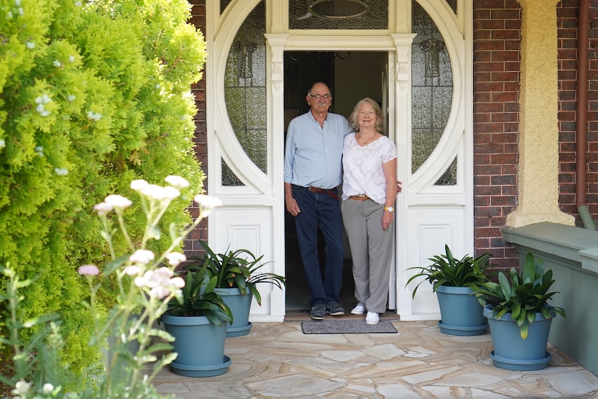 Un hombre y una mujer mayores se encuentran en la puerta de su casa.