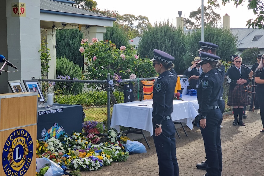 Three police officers salute a memorial to a fallen police officer.