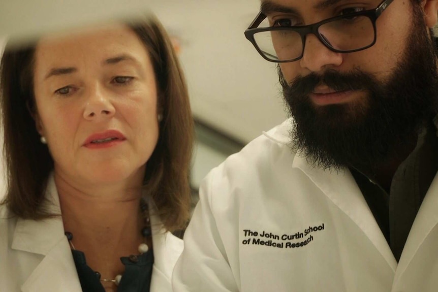 Female professor standing next to a male colleague, both in lab coats.