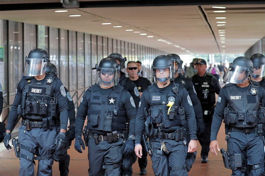 A group of police officers wearing helmets walk through a metro station.