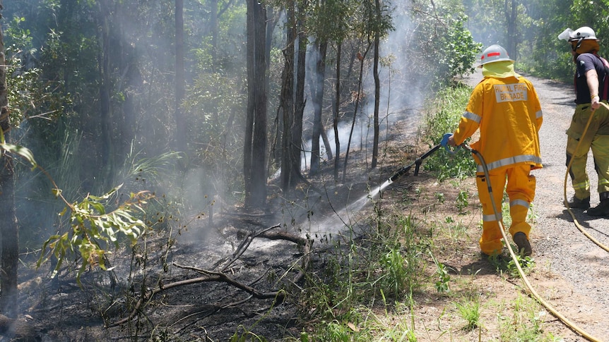 Two firefighters stand with a hose as they control a small fire in a bushland area