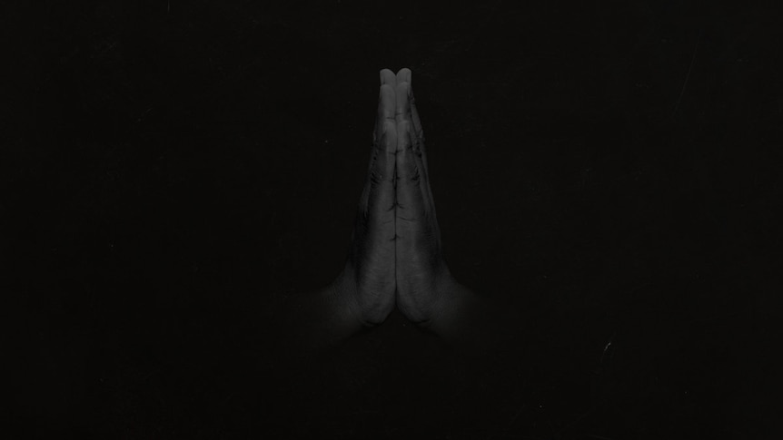 Two hands joined together as if in prayer, against a black background