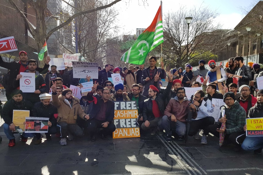 A large group of protesters pose for photos, while holding signs