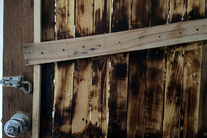 Un primer plano de una puerta de entrada de madera marrón que se mantiene unida mediante clavos plateados.  Hay huecos en los tablones.