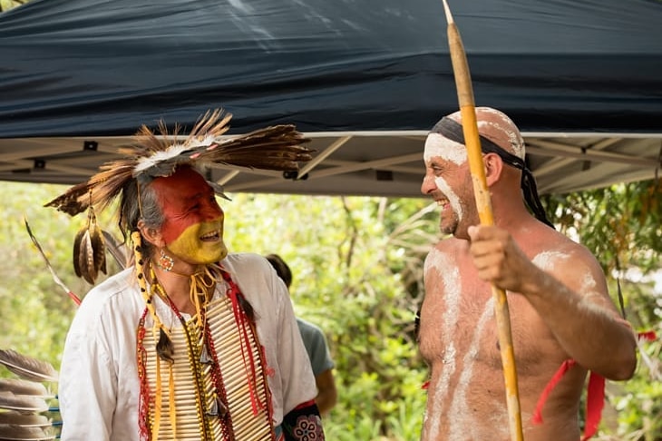 A Native American man and an Aboriginal man wearing their traditional face paint look at each other and smile