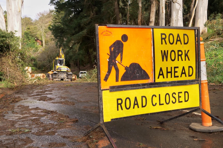 A 'ROAD WORK AHEAD' sign is laid out on a muddy road, with trucks visible further down.