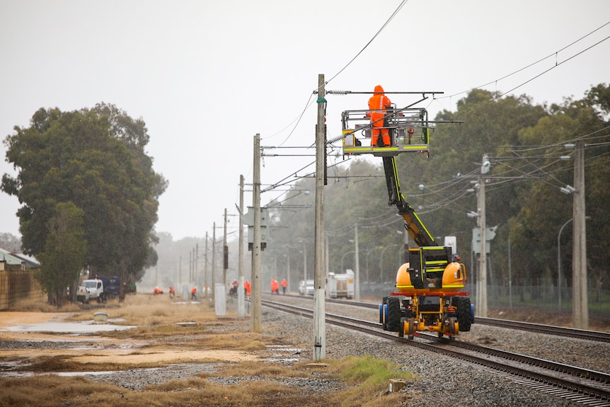 A man on a large crane works on overhead powerlines.