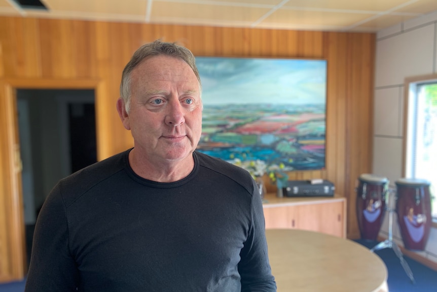 A man in a black shirt stands in front of a painting