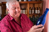 An older fellow smiles while looking at a blue antique bottle.