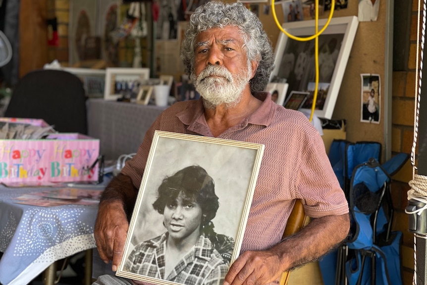 man in pink collar shirt holds black and white photo of his nephew.