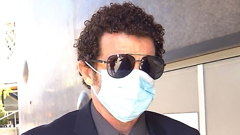 A curly-haired man wearing sunglasses and a mask.