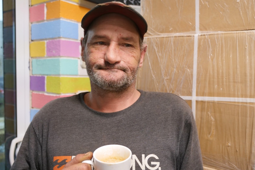 A man stands in front of a wall with a coffee