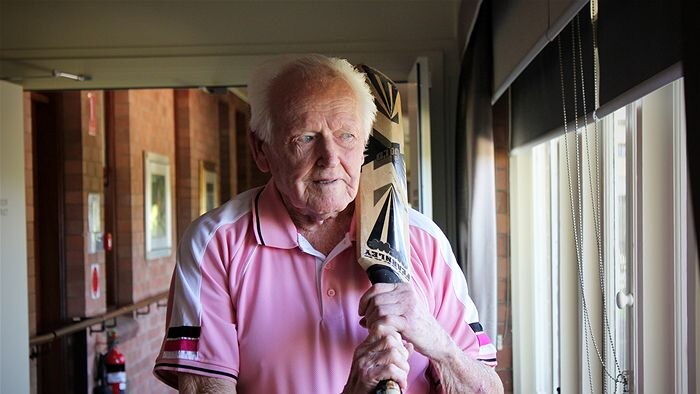 Image of 100-year-old Harold Stapleton in pink cricket shirt, with cricket bat held over his shoulder