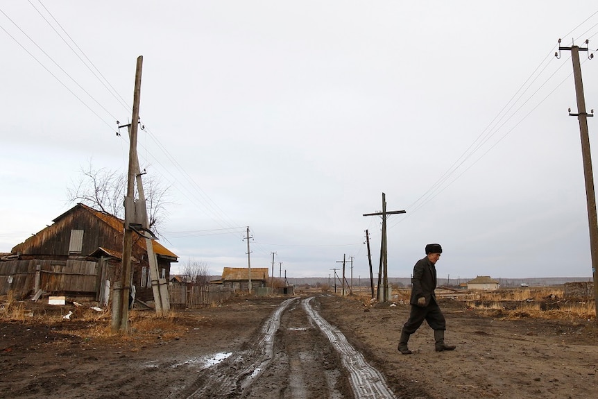 A man walks next to his old house in the abandoned village of Muslyumovo, Russia.