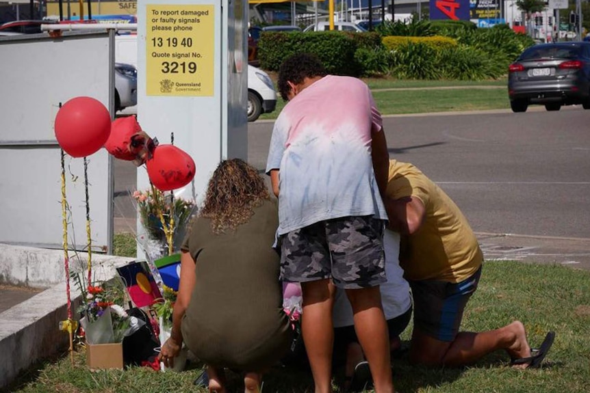 A woman, man and young boy pay their respects at a roadside memorial near a busy intersection in Townsville.