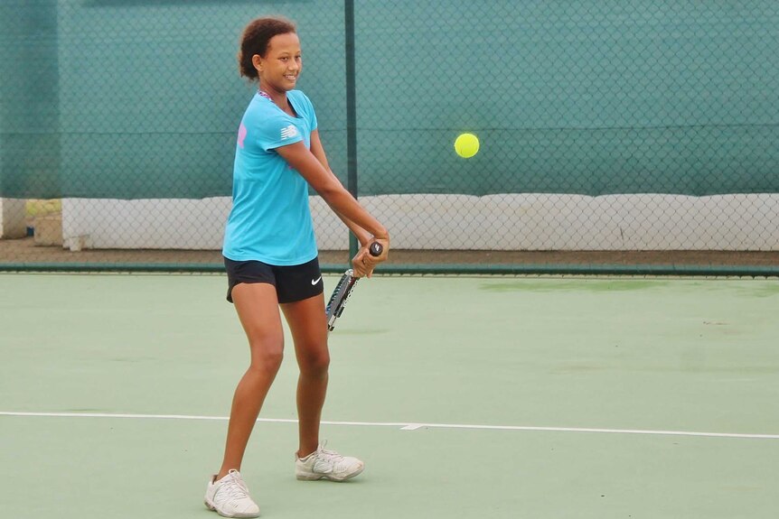 A girl smiles as the prepares to hit an aggressive backhand on the tennis court.