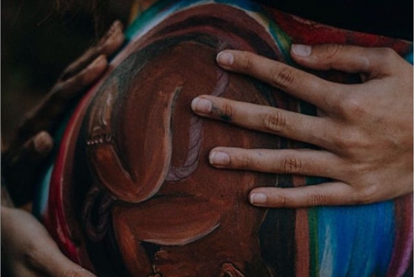 Four hands on a pregnant belly which has a baby painted on it