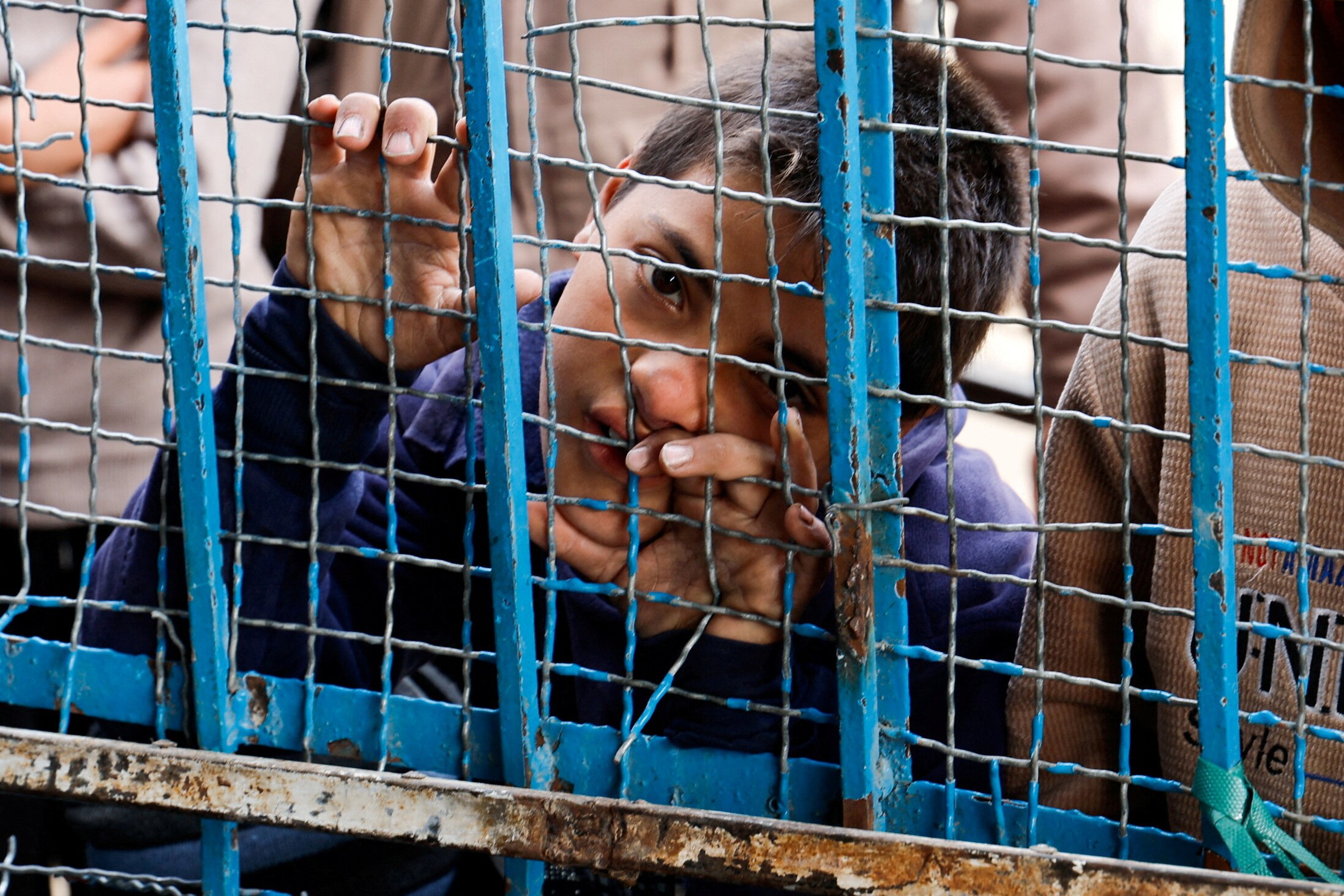 A young boy behind a steel grate fence waiting for food.