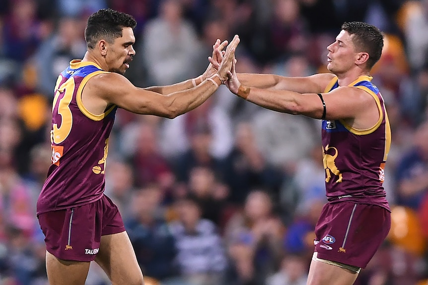 Two Brisbane Lions AFL players high five each other after a goal was kicked.