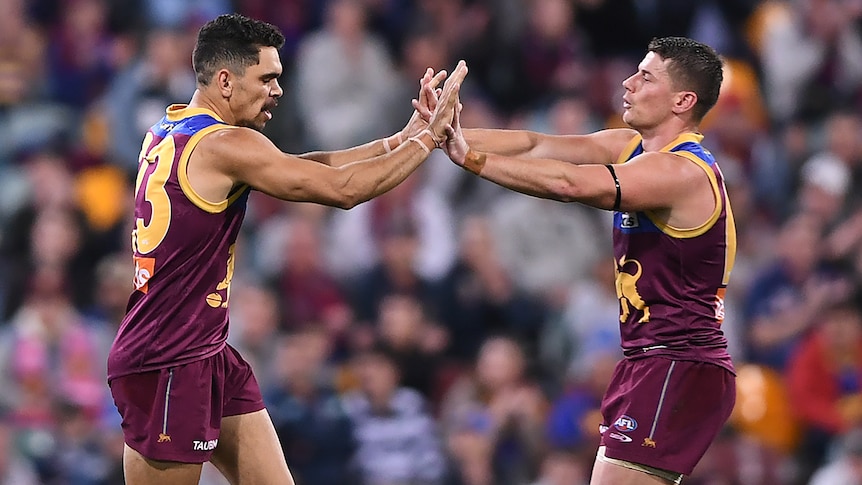 Two Brisbane Lions AFL players high five each other after a goal was kicked.