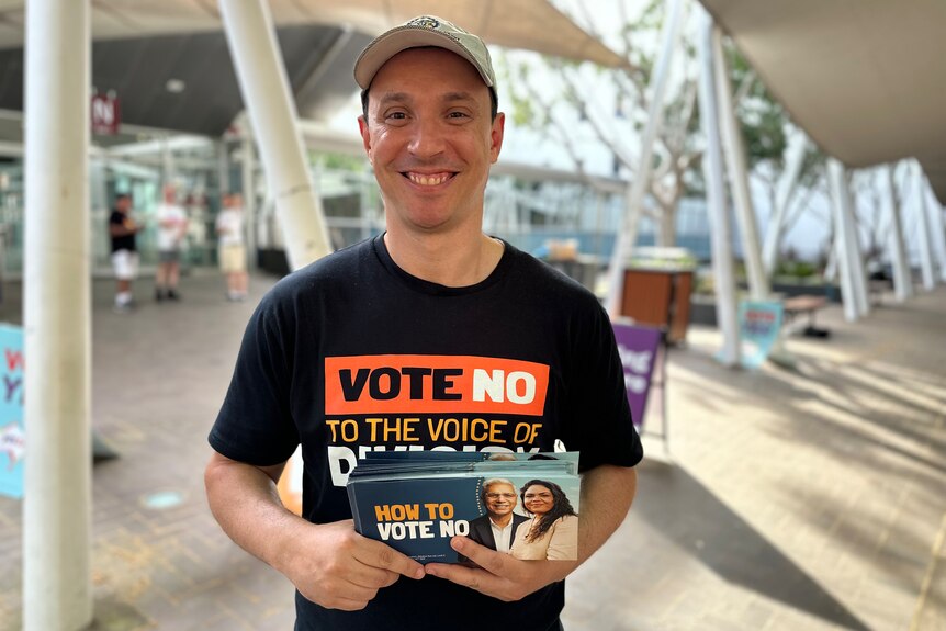 A man in a cap wears a Vote No t-shirt and holds a vote No card at a polling station in Sydney. 