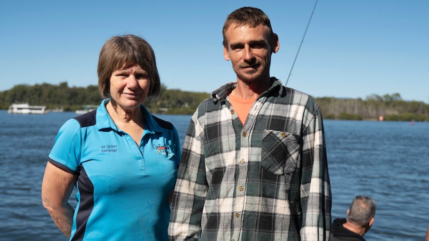 A woman in a blue shirt and a man in a flannel shirt stand side by side on a boat.