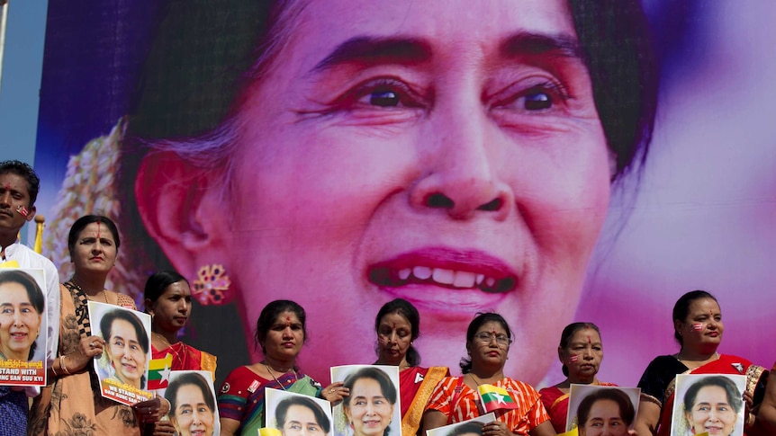 A group of people hold portraits of Myanmar leader Aung San Suu Kyi in front of a large photo of her.