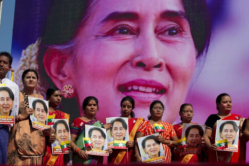 A group of people hold portraits of Myanmar leader Aung San Suu Kyi in front of a large photo of her.