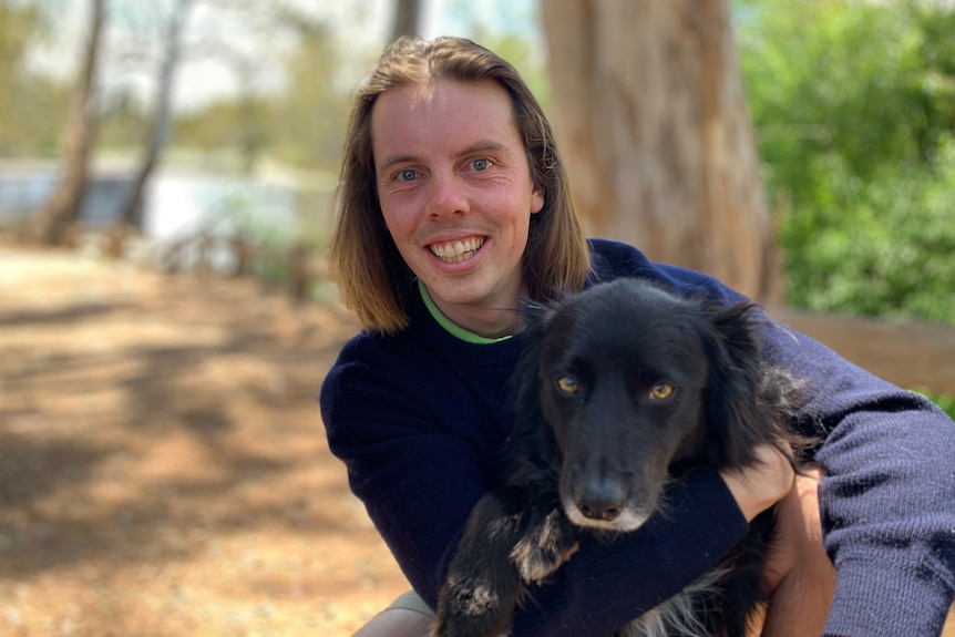 A young man cuddles a black border collie.