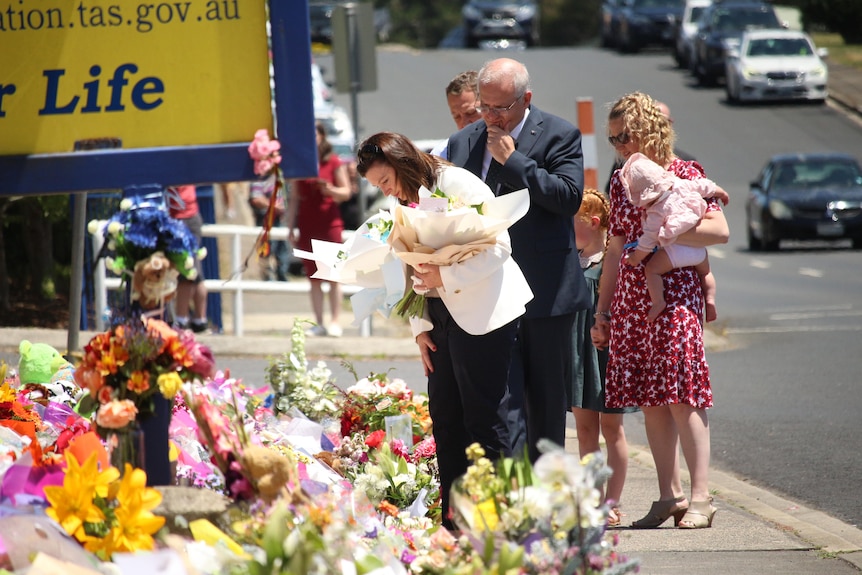  A woman holding flowers with a suited man walk along a flower tribute