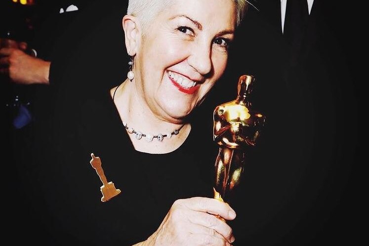 A woman smiles as she holds an Academy Award.