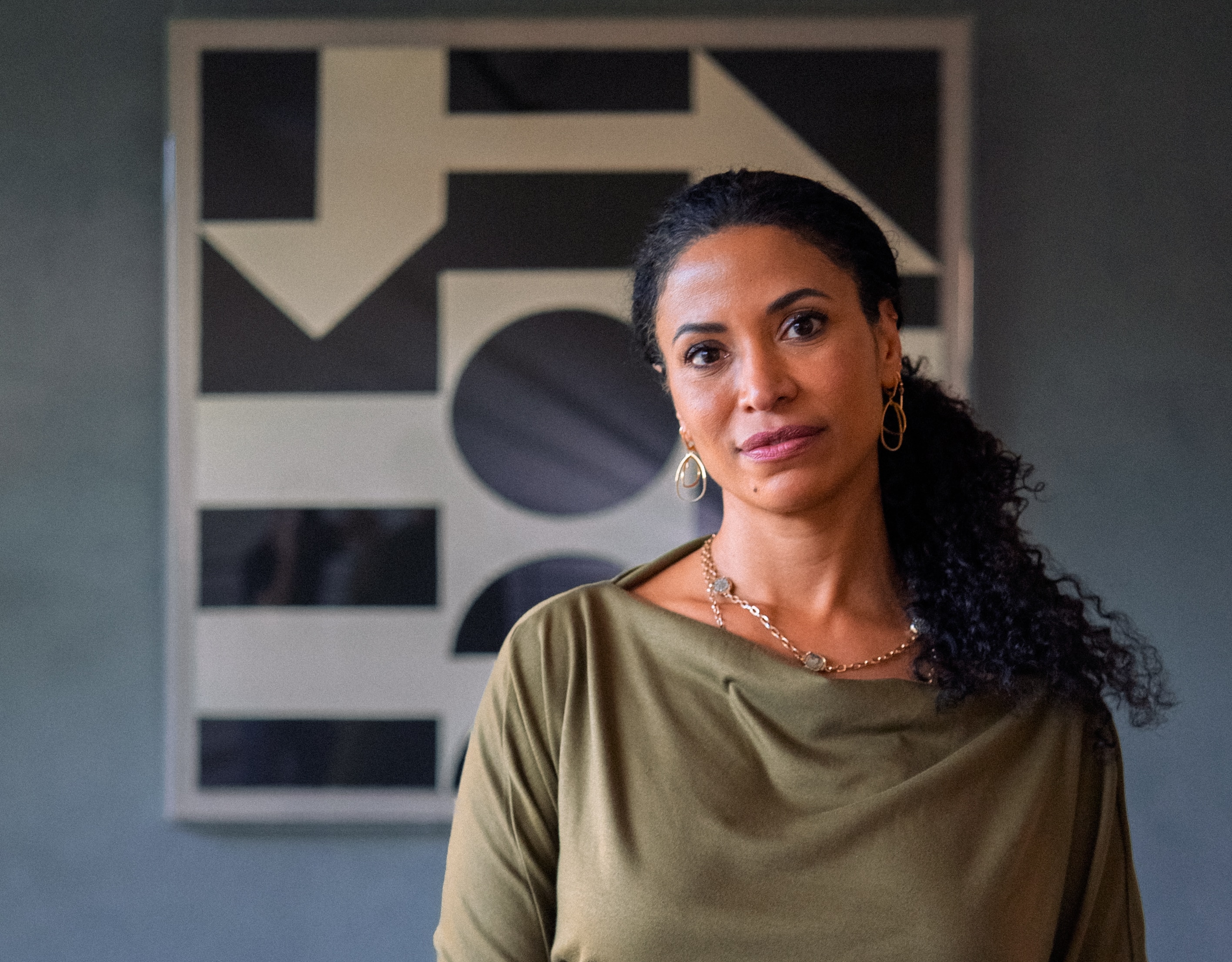 A young, dark-haired woman stands in front of a an artwork on a wall.
