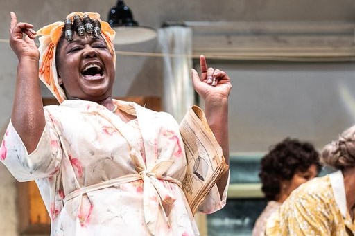 A black woman with rollers in her hair with arms raised and mouth wide open