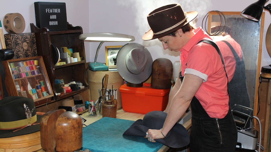 Woman leans over table moulding a felt hat in her hands.